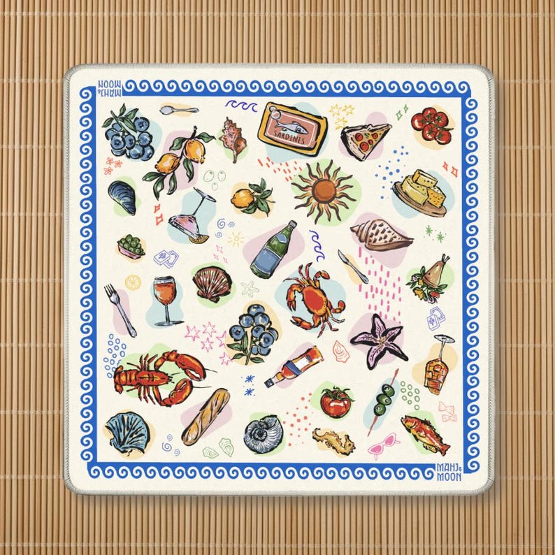 May include: A square off-white textile mat featuring a blue Greek key border and the text MAHJ & MOON. The surface is decorated with colorful illustrations of seafood, fruit, vegetables, wine glasses, a sun, and various shells in a scattered pattern.