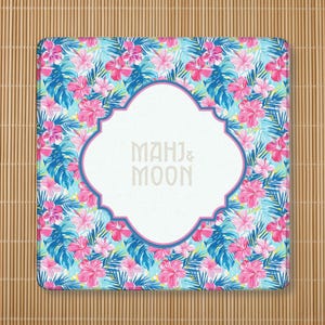 May include: Square coaster with a tropical floral pattern featuring pink hibiscus flowers, blue and green leaves, and the text "MAHJ & MOON" in a white, ornate frame.