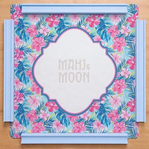 May include: A decorative tray with a floral pattern featuring pink hibiscus flowers and blue tropical leaves. The tray has a white centre with the text "MAHJ & MOON" and is framed by a light blue border.