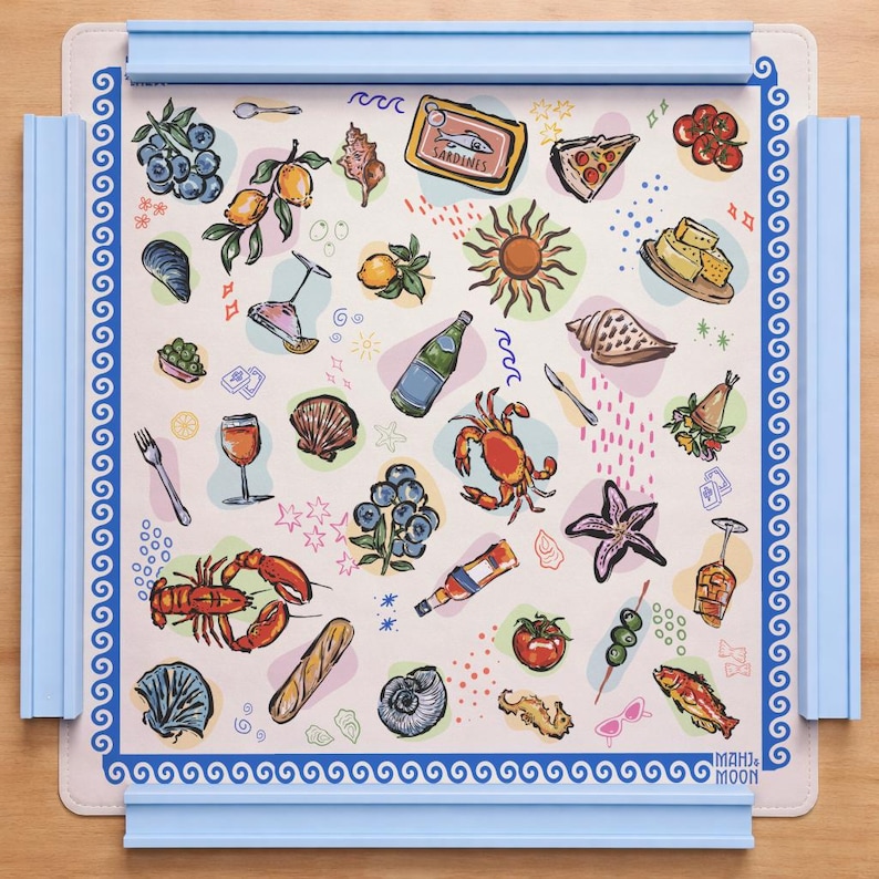 May include: A square game mat with a light cream background featuring colorful illustrations of seafood, fruit, drinks, and Mediterranean-themed items. The mat has a blue Greek key border and four light blue plastic rails attached to the edges.