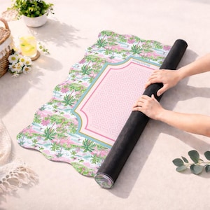 May include: A rectangular mat with a scalloped edge featuring a tropical palm tree pattern in shades of green and pink. The centre has a pink rectangular panel with a white Greek key border and the text "Mah&eacute; Moon" printed in small letters.