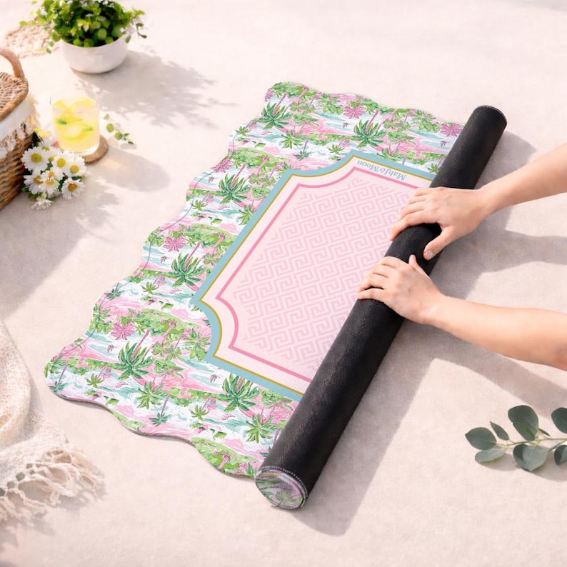 May include: A rectangular mat with a scalloped edge featuring a tropical palm tree pattern in shades of green and pink. The centre has a pink rectangular panel with a white Greek key border and the text "Mah&eacute; Moon" printed in small letters.