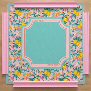 May include: A square mahjong mat featuring a pink background with a repeating pattern of yellow lemons, green leaves, and small white and pink flowers. A central teal panel with a subtle leaf texture is framed by pink lines with the text MAHJ & MOON.