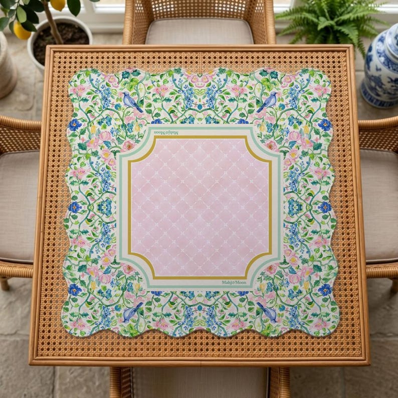 May include: A square scalloped-edge mat featuring a central light pink diamond-patterned panel framed by a gold and light green border. The outer border displays a floral pattern with blue birds, pink flowers, and green vines with the text MahjongMoon.