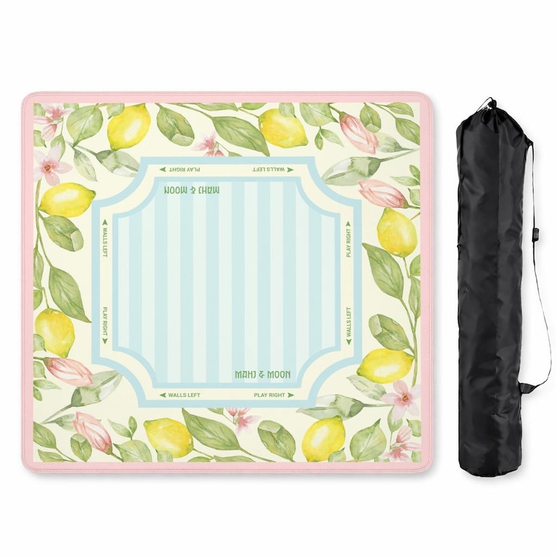 K&ouml;nnte beinhalten: Eine quadratische Mahjong-Matte mit rosa Rand, verziert mit Aquarell-Zitronen, Bl&auml;ttern und rosa Bl&uuml;ten. Die Mitte hat ein hellblaues Streifendesign mit Text. Eine schwarze Tragetasche befindet sich auf der rechten Seite.