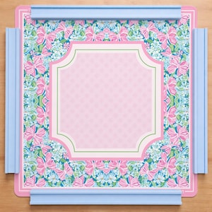 Könnte beinhalten: Ein dekoratives rosa und blaues Tablett mit einem Blumen- und Schmetterlingsmuster. Das Tablett hat eine rosa Mitte mit einem weißen und grünen Rand. Hellblaue Schienen sind an den Rändern des Tabletts befestigt.