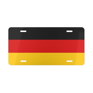 Puede incluir: Placa de matrícula rectangular con la bandera alemana. La placa está dividida en tres franjas horizontales: negro en la parte superior, rojo en el medio y amarillo en la parte inferior. Tiene cuatro orificios de montaje.