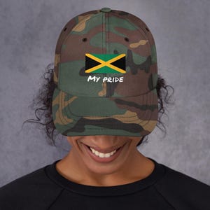 Puede incluir: Gorra de béisbol de camuflaje con la bandera jamaicana y el texto blanco "MY PRIDE". La gorra tiene una visera curva y un diseño clásico de seis paneles. Los colores de la bandera son verde, amarillo y negro.