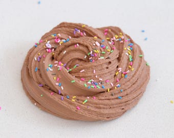 Puede incluir: Slime marrón con chispas de colores. El slime tiene forma de espiral y parece suave y pegajoso.