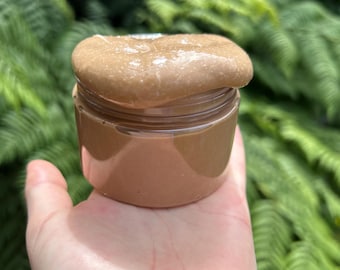 May include: A brown slime in a clear plastic jar. The slime is smooth and glossy, and it appears to be very thick.