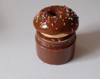 Puede incluir: Una dona de chocolate con chispas de colores se sienta encima de un frasco de vidrio lleno de crema de chocolate.