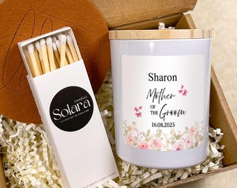 May include: A gift box containing a white candle with a wooden lid, a box of matches, and a round brown felt coaster. The candle label features the text Sharon, Mother of the Groom, 16.08.2025, and pink floral graphics. The matchbox is labeled Solara.