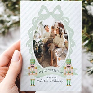 May include: A Christmas card with a family photo in a light green oval frame. The card reads "Merry Christmas from the Anderson Family" and features nutcracker illustrations. The background has a striped pattern.