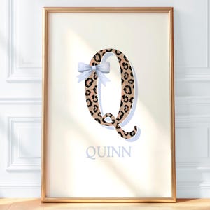 May include: Framed print featuring the letter "Q" in a leopard print design, adorned with a light blue bow. The name "Quinn" is printed in a soft gray font below the letter. The artwork is set in a gold frame.