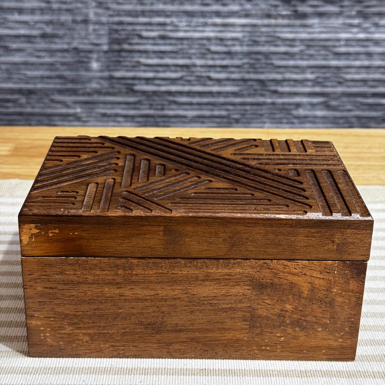 May include: A wooden box with a geometric pattern carved into the lid. The box is a dark brown color and has a smooth finish.