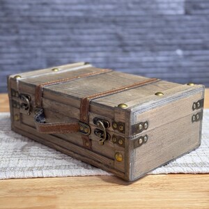May include: A wooden box with a brown leather strap and brass hardware. The box has a distressed finish and is closed.