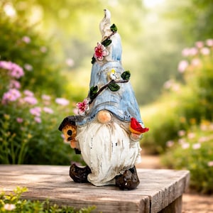 May include: A garden gnome statue with a blue hat adorned with pink flowers and green leaves. The gnome has a long white beard, a small birdhouse, and a red bird perched on its hand. The statue is placed on a wooden surface.