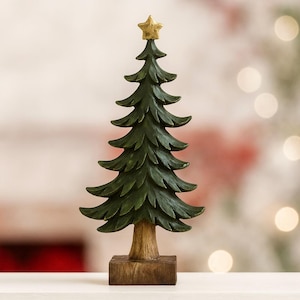 Könnte beinhalten: Dekorative Weihnachtsbaumfigur. Der Baum ist dunkelgrün mit einem goldenen Stern an der Spitze. Er hat einen Holzsockel und -stamm. Der Baum ist etwa 20 cm hoch.