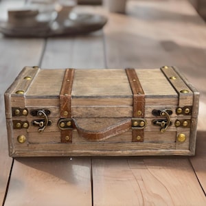 May include: A wooden box with a leather handle and brass accents. The box has a distressed finish and is decorated with leather straps.