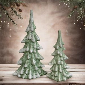 May include: Two ceramic Christmas trees in a green and white glaze. The larger tree is taller than the smaller tree.