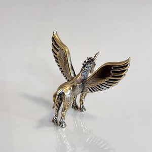 Puede incluir: Peque&ntilde;a y detallada figura de un unicornio alado, o pegaso, con acabado en bronce. La escultura presenta intrincados detalles en las alas, la melena y el cuerpo, con un aspecto ligeramente envejecido. El unicornio se alza sobre cuatro patas, con las alas extendidas.