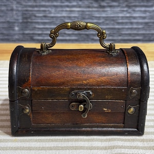 May include: A small wooden treasure chest with a brass handle and latch. The chest is brown with a dark wood grain and has a distressed finish.