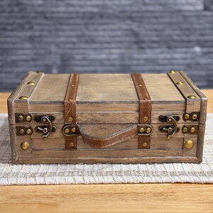 May include: A wooden box with a leather handle and brass accents. The box has a distressed finish and is decorated with leather straps.