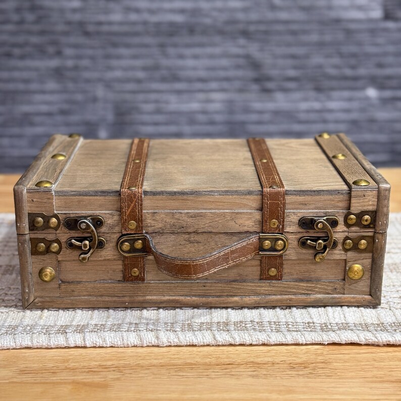 May include: A wooden box with a leather handle and brass accents. The box has a distressed finish and is decorated with leather straps.