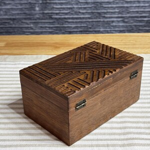 May include: A wooden box with a geometric pattern carved into the lid. The box has two brass hinges on the side.