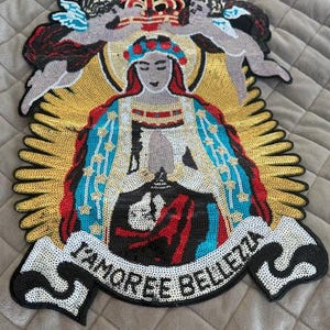 May include: A sequined patch featuring a religious figure with a crown, surrounded by angels and a golden halo. The figure wears a blue and red robe. The banner below reads "L'AMOREE BELLEZZA".