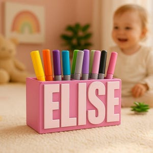 Könnte beinhalten: Ein rosa Stifthalter mit dem Namen "ELISE" in weißen Blockbuchstaben. Der Halter enthält eine Vielzahl farbiger Marker. Ein Kind ist im Hintergrund unscharf.