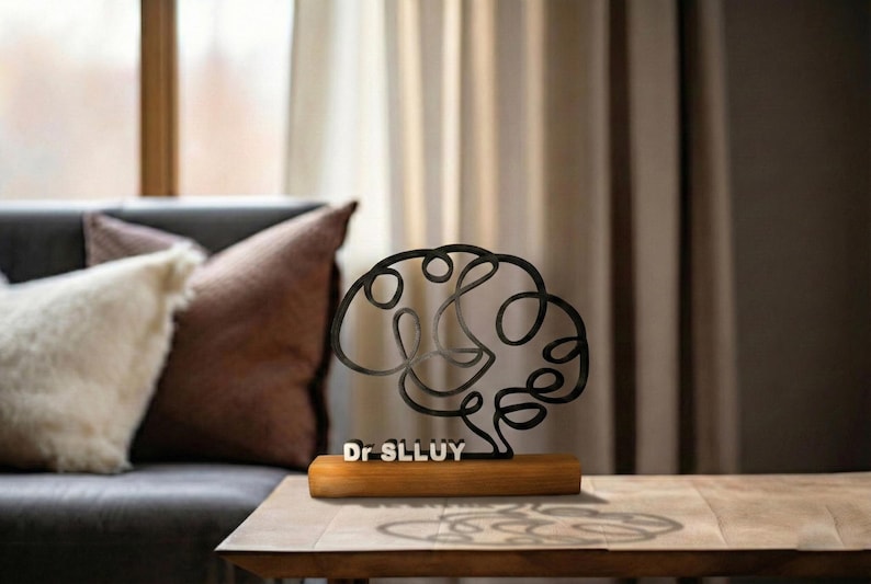 Puede incluir: Una escultura de alambre de metal negro con forma de cerebro humano, montada sobre una base rectangular de madera. La base presenta el texto blanco Dr SLLUY. La escultura est&aacute; compuesta por una l&iacute;nea continua que forma el cerebro.