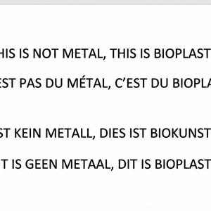Puede incluir: Un letrero rectangular blanco con cuatro l&iacute;neas de texto en negro. El texto dice: THIS IS NOT METAL, THIS IS BIOPLASTIC; CECI N&rsquo;EST PAS DU M&Eacute;TAL, C&rsquo;EST DU BIOPLASTIQUE; DIES IST KEIN METALL, DIES IST BIOKUNSTSTOFF; DIT IS GEEN METAAL, DIT IS BIOPLASTIC.