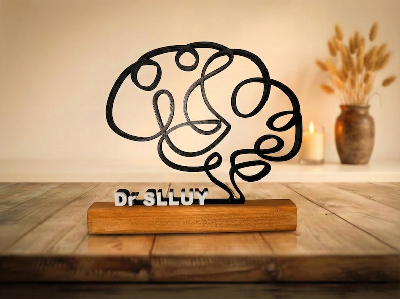 Puede incluir: Una escultura de l&iacute;nea continua negra con forma de cerebro humano, montada sobre una base rectangular de madera. El texto blanco Dr SLLUY est&aacute; fijado en la parte frontal de la base, posicionado directamente bajo la estructura cerebral.