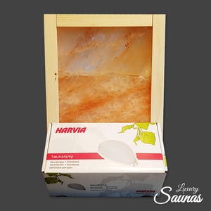 Könnte beinhalten: Eine weiße Box mit dem Harvia-Logo und dem Text "Saunalamp" darauf. Die Box steht vor einem Holzrahmen mit einem großen Stück Himalaya-Salz darin. Das Salz ist hellorange mit weißen Streifen.