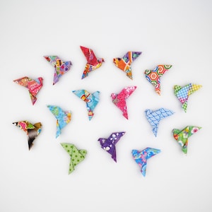 May include: A collection of colourful origami birds arranged on a white surface. The birds are crafted from patterned paper in various colours, including red, blue, green, and purple. Each bird has a unique design, showcasing a variety of patterns and textures.