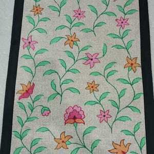 May include: Rectangular beige rug with a black border, featuring a floral pattern. The design includes pink and orange flowers with green leaves and stems, creating a natural, decorative aesthetic.
