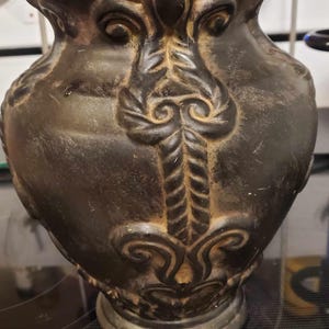May include: A black ceramic vase with intricate gold-colored designs. The vase has a wide base and a narrow neck.
