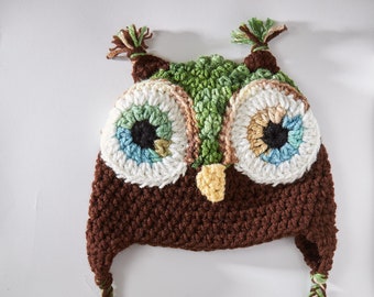 May include: Brown crocheted owl hat with green, blue, and white accents. The hat has long braided ties.