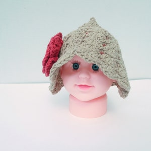 Op de afbeelding: Een handgemaakte, beige gehaakte hoed met een rode bloem. De hoed heeft een puntige kroon en een brede rand. Deze babyhoed is een uniek, handgemaakt accessoire.
