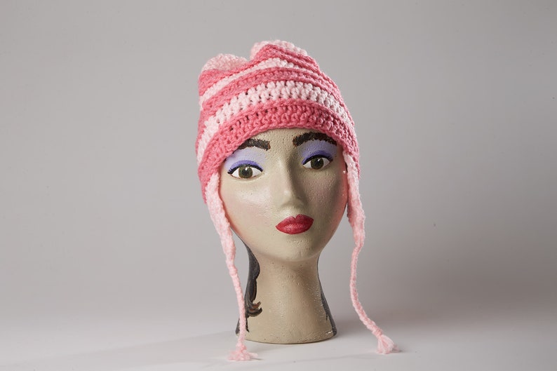 May include: Pink and white striped crocheted hat with long ties. The hat is on a mannequin head.