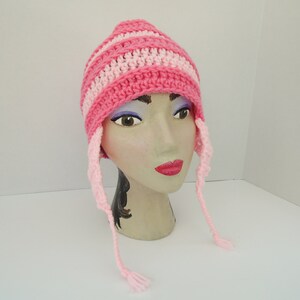 May include: Pink and white striped crocheted hat with long ties. The hat is on a mannequin head.