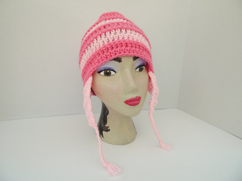 May include: Pink and white striped crocheted hat with long ties. The hat is on a mannequin head.