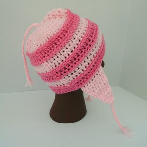 May include: Pink and light pink striped crocheted hat with a long tail. The hat is on a brown mannequin head.