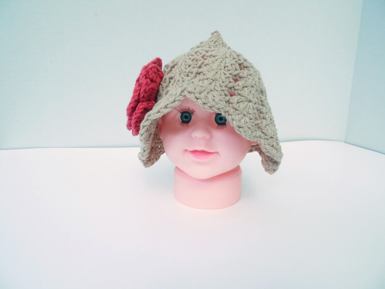 Op de afbeelding: Een handgemaakte, beige gehaakte hoed met een rode bloem. De hoed heeft een puntige kroon en een brede rand. Deze babyhoed is een uniek, handgemaakt accessoire.
