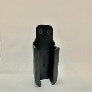 以下が含まれることがあります： 長方形のボディと上部と下部が開いた黒色の3Dプリントホルスター。ホルスターの上部には2本のネジがあり、側面には「YPK666」の文字があります。ホルスターはアイテムを保持するように設計されています。