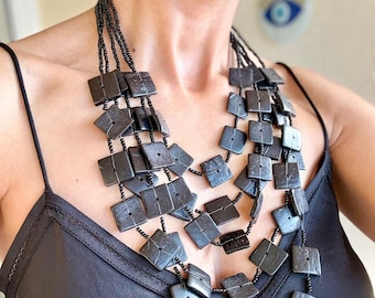 Collar babero geométrico negro, joyería llamativa con cuentas cuadradas grandes, gargantilla moderna de múltiples hebras con diseño arquitectónico.
