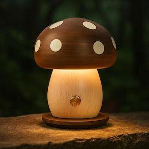 May include: A mushroom-shaped table lamp with a brown cap featuring white polka dots. The stem is light-colored wood, and the lamp emits a warm glow. The lamp sits on a round wooden base.
