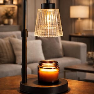 May include: A black metal candle warmer lamp with a clear, textured glass shade and a lit candle in a glass jar. The lamp has a curved arm and sits on a round base. The warm light creates a cozy ambiance.
