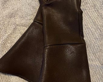 May include: A pair of brown leather gloves with long cuffs. The gloves have a textured surface and are folded in half.
